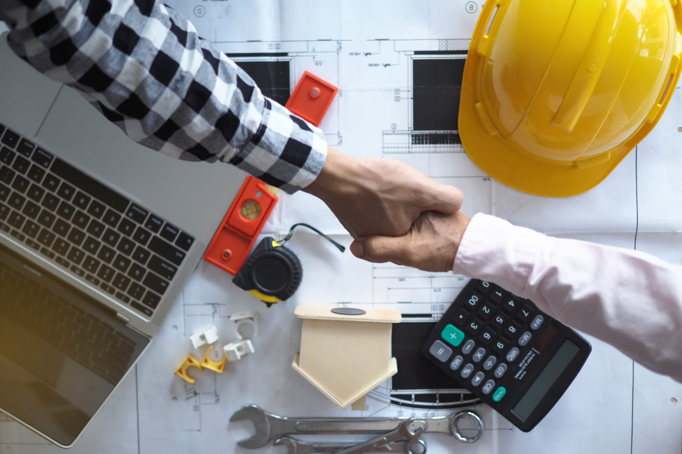 Deux hommes qui se serrent la main au-dessus de plans de construction.